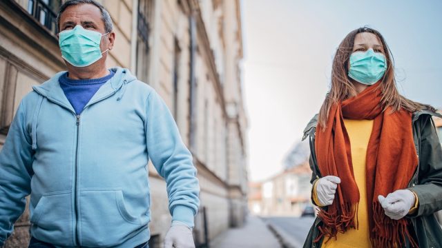 older white man and woman with masks walking outside