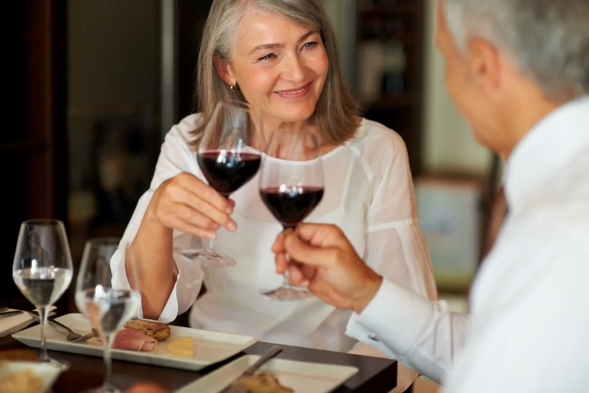 older white couple toasting red wine at dinner