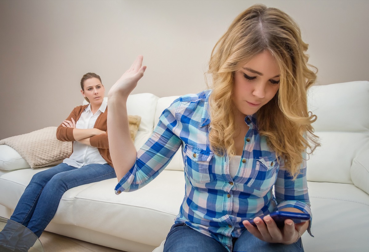 white teen girl texting and putting her hand up to ignore her mom in the background