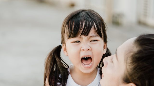 young asian girl screaming while mother crouches next to her