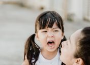 young asian girl screaming while mother crouches next to her