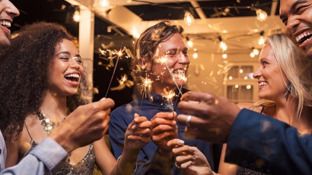 multiracial group of 30-something friends celebrating new year's eve with sparklers