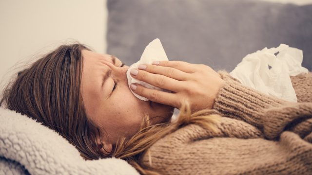 a sick woman on a couch blowing her nose with a tissue, skin cancer facts