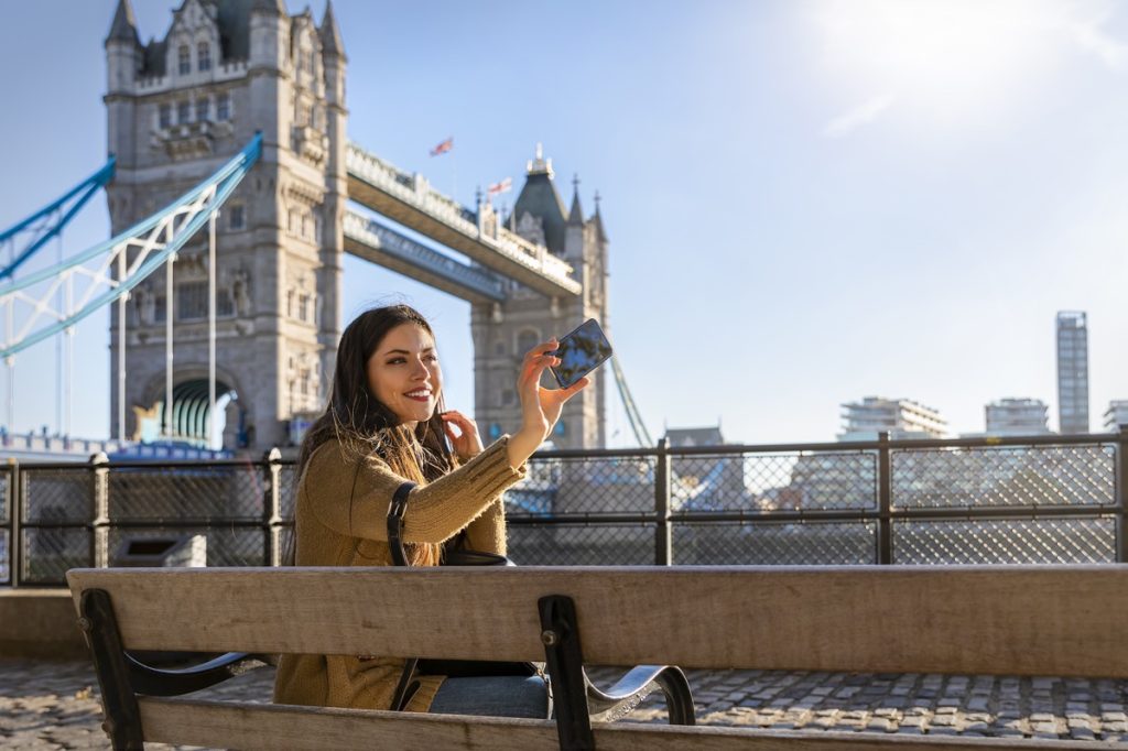 beautiful female London traveler takes a selfie picture with her phone in front of the Tower Bridge on a sunny day