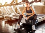 Asian young woman tired taking a break from running or exercise sitting on treadmill machine drinking water and towel sweat in fitness gym healthy .girl in sportswear workout rest in morning