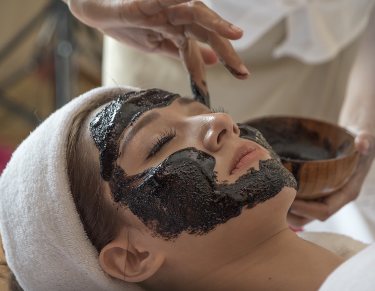 Young beautiful woman is having a black charcoal mask on her skin. Skincare and spa treatment