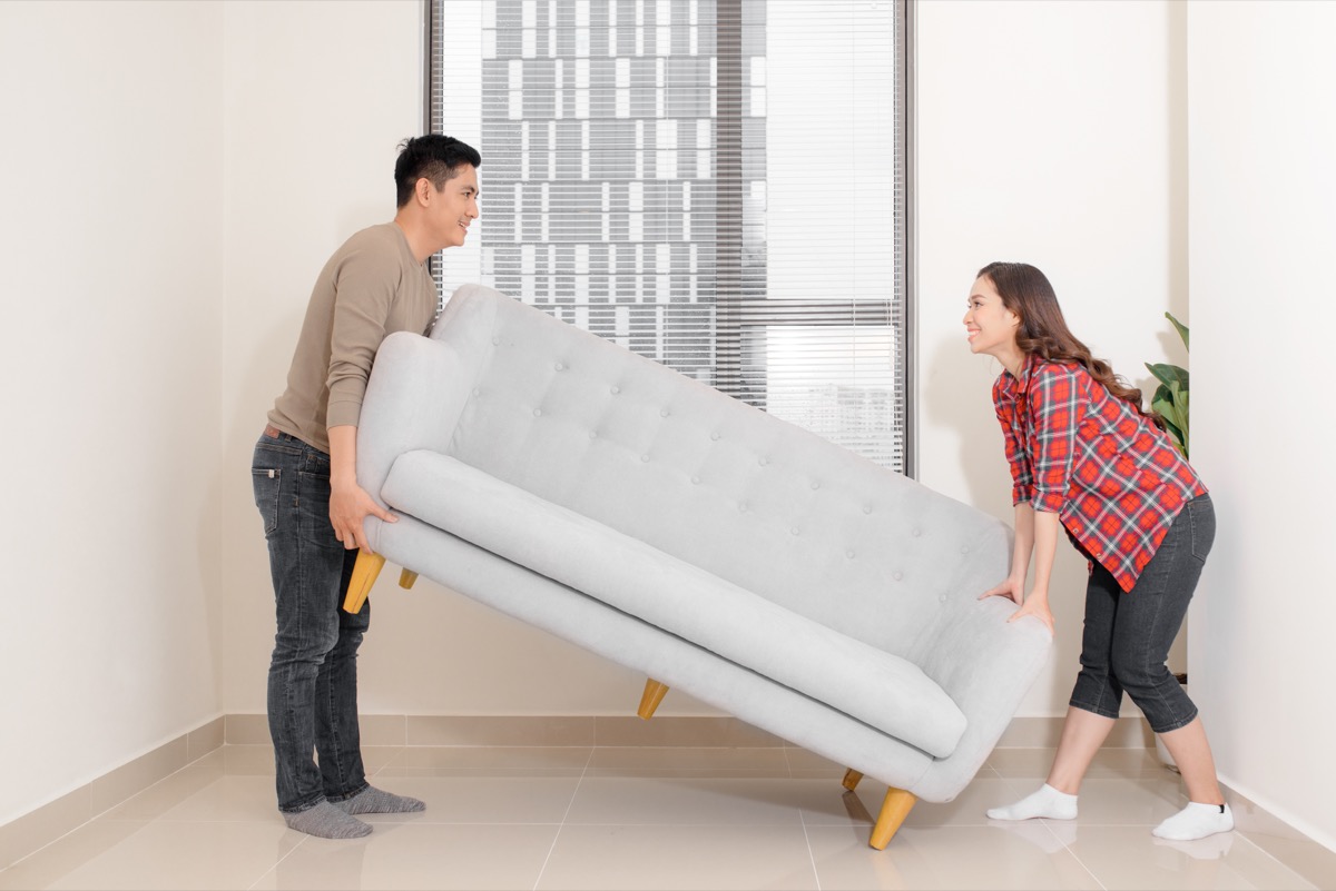 Couple rearranging furniture in their living room moving a couch together