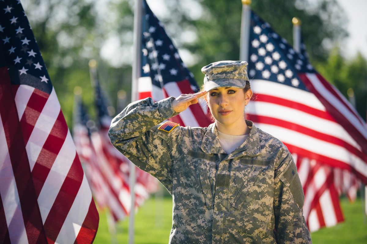 Female Soldier in uniform saluting in front of American flags