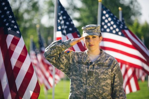 Woman soldier saluting in front of American flags