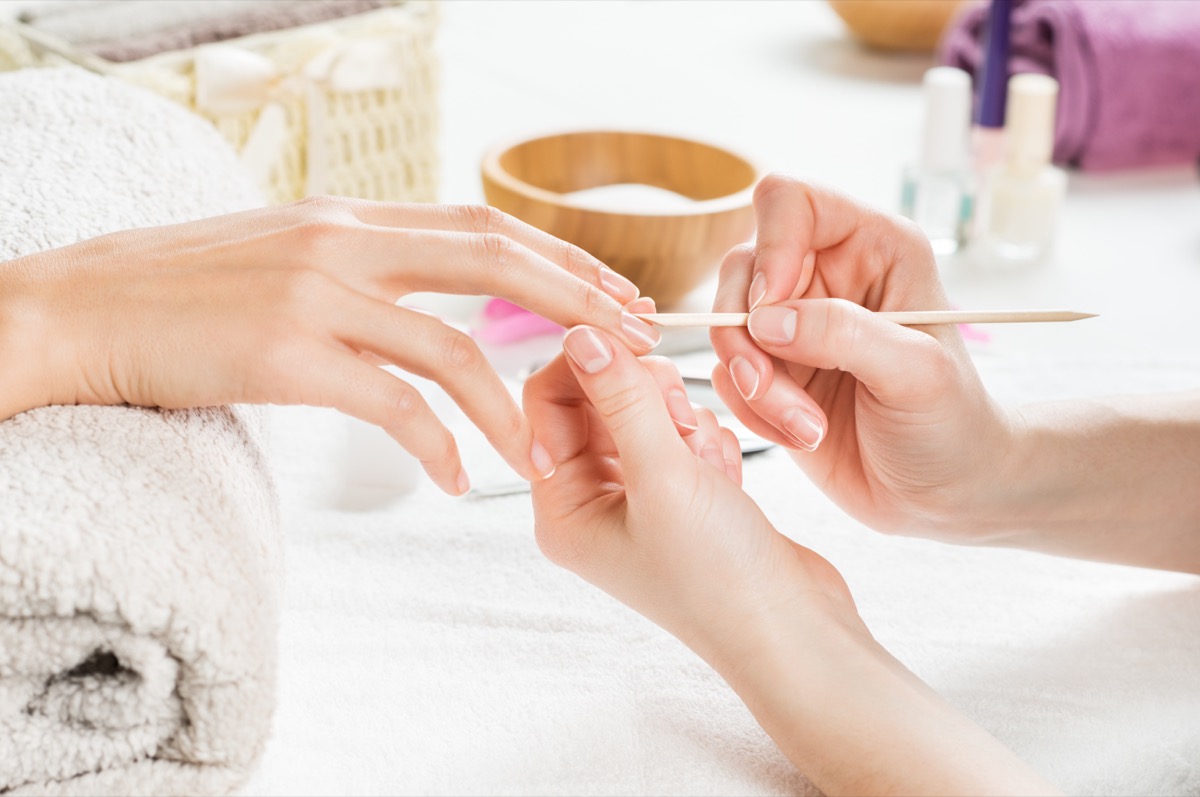 Closeup shot of a woman using a cuticle pusher to give a nail manicure. Nail technician giving customer a manicure at nail salon. Young caucasian woman receiving a french manicure