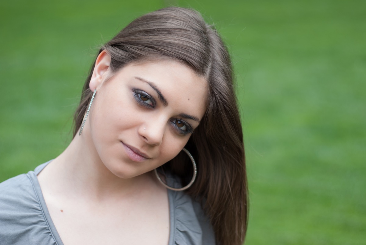 girl posing for photo in grass wearing large hoop earrings and a gray top