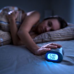 woman hitting alarm clock at 5 a.m. in the dark
