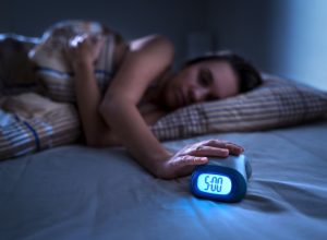 woman hitting alarm clock at 5 a.m. in the dark