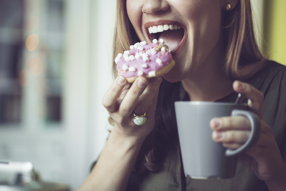 close up of young white woman eating pink frosted donut with her coffee