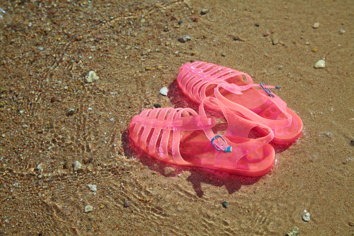 Pink Women's JELLY SANDALS on a sea shore. LADIES FLAT JELLIES SUMMER BEACH SHOES. Sand background - Image