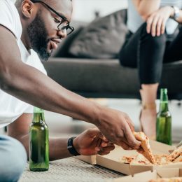 man eating pizza and drinking beer on floor, healthy sex after 40