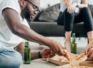 man eating pizza and drinking beer on floor, healthy sex after 40