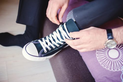 man putting on converse shoes while wearing a suit