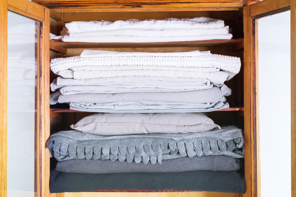 stack monochrome white gray dark grey bed, linen pillowcases cushion in wooden old retro wardrobe cabinet furniture storage interior closeup country style retro
