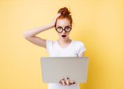 shocked woman with red hair holding a laptop against an orange background