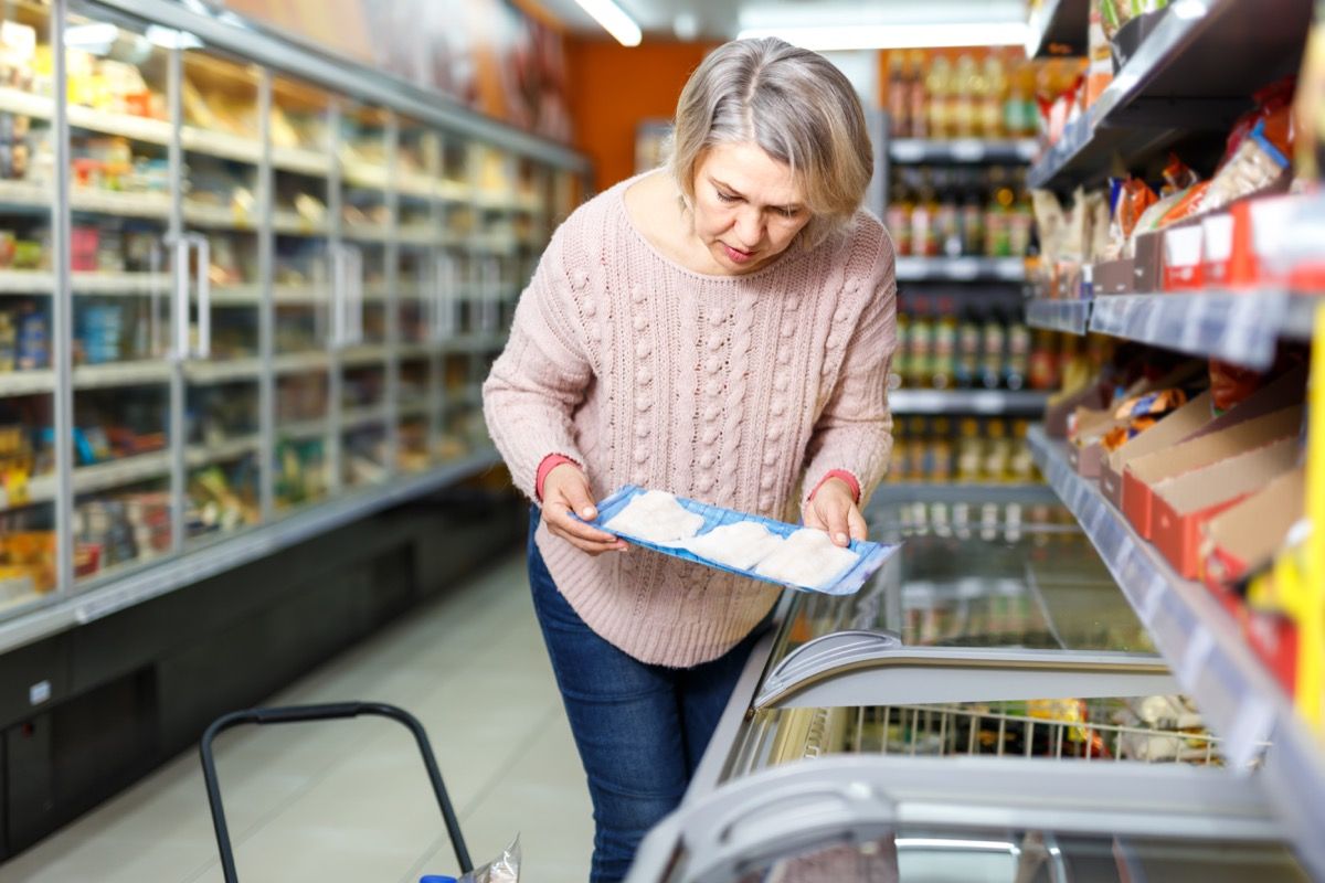 Middle-aged woman buying frozen fish at the grocery store