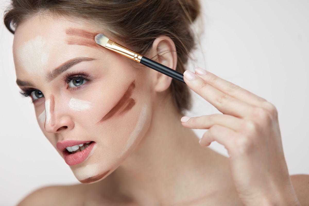 Beauty Makeup. Portrait Of Beautiful Young Female With Smooth Skin And Fresh Makeup And Hands With Brush Applying Make-Up Product, Conturing And Highlighting Lines On Woman Face