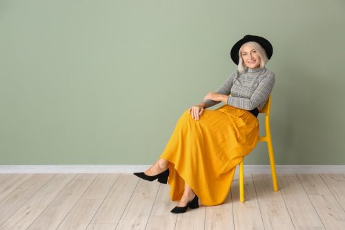Woman in 40s sitting in a chair wearing a bold bright yellow skirt outfit with a hat