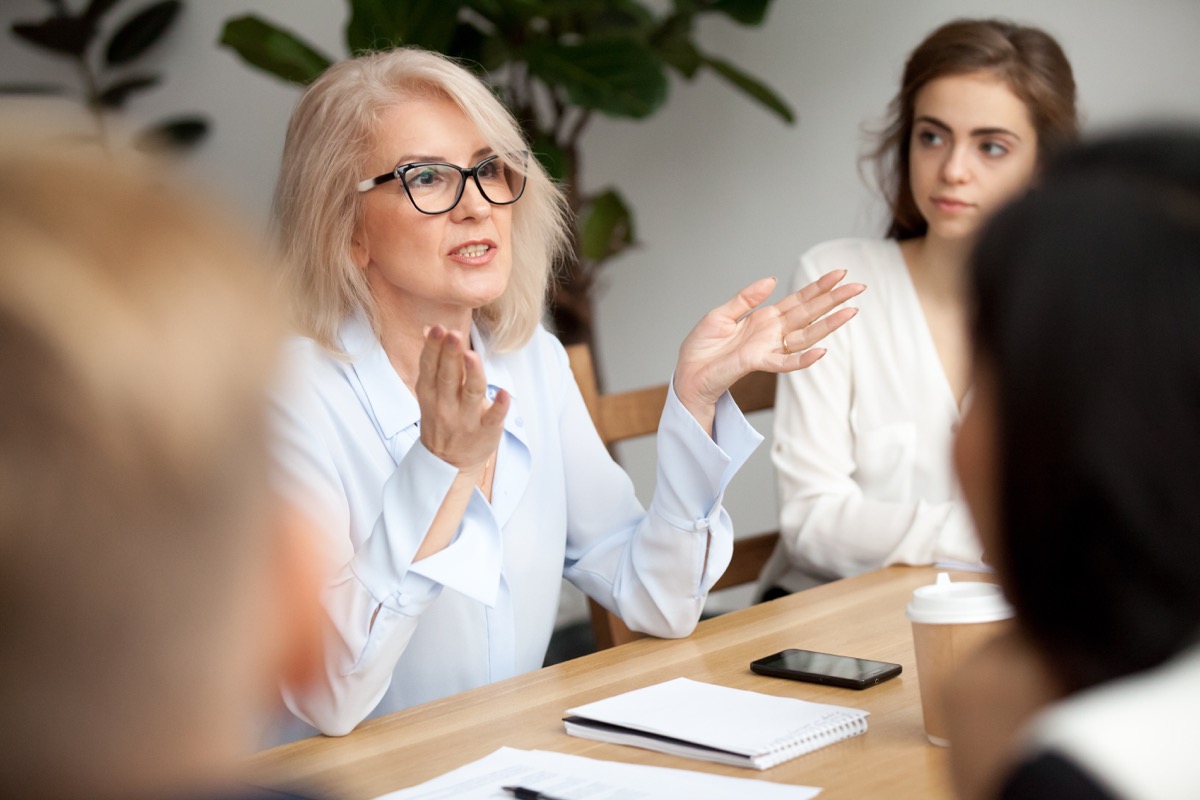 Femeie de afaceri în vârstă atrăgătoare, profesor sau antrenor mentor vorbind cu tinerii, purtând ochelari bătrâni care studiază publicul la seminarul de formare, lider de afaceri vorbind la întâlnire