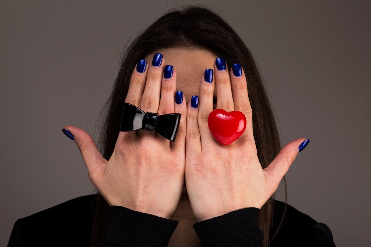 a woman wearing a black bow ring and red heart ring cover her face with her hands