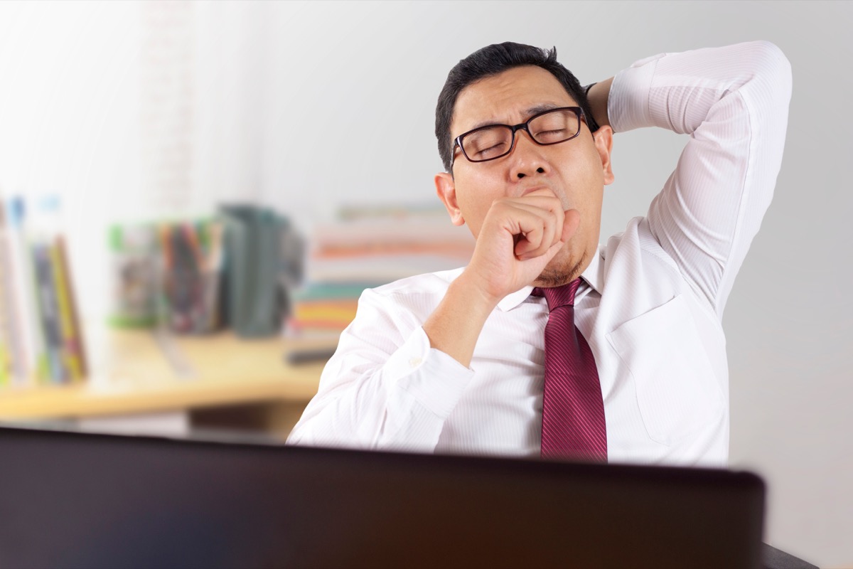 Asian Man Sitting at His Desk at Work Yawning Signs of Burnout