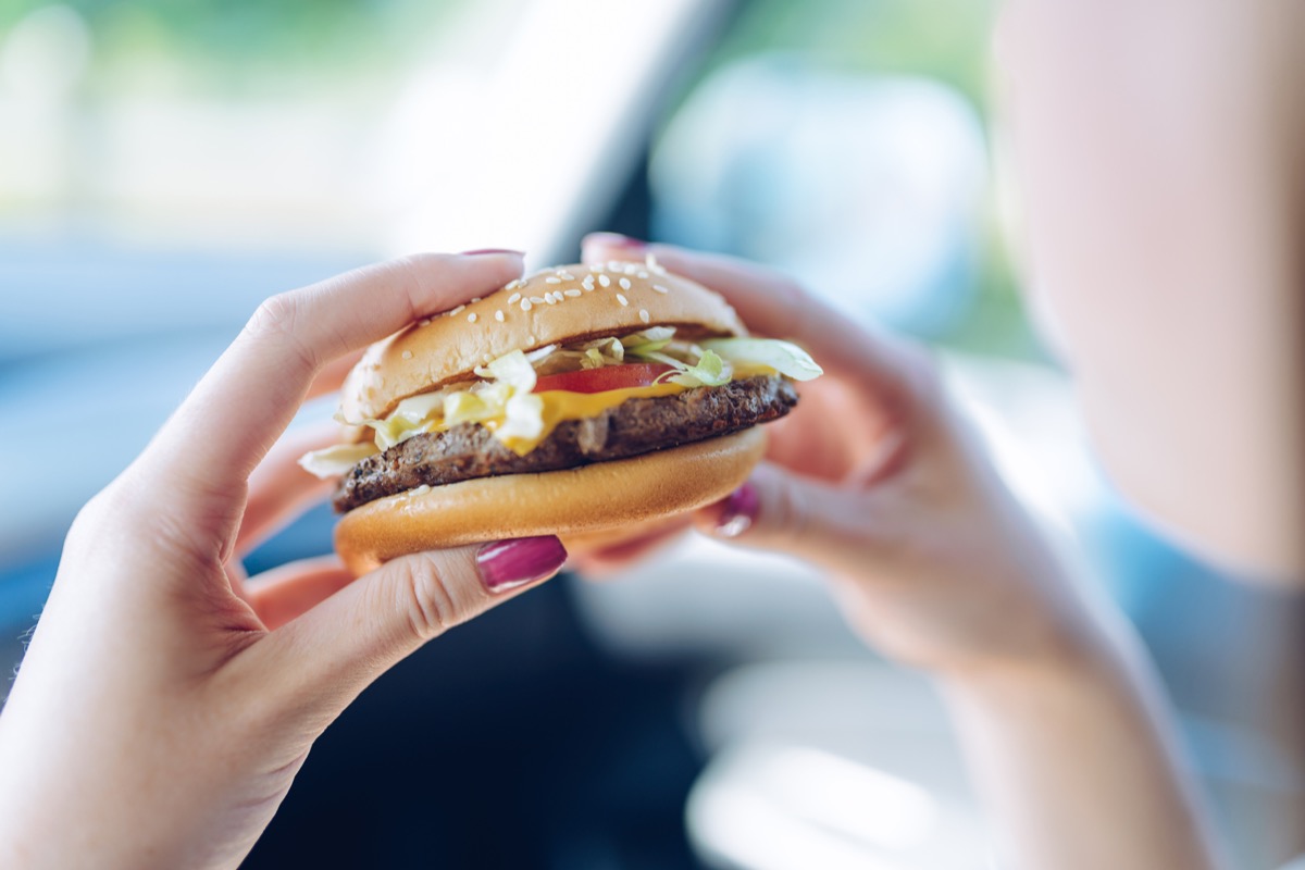 Girl holding a fast food burger in the car