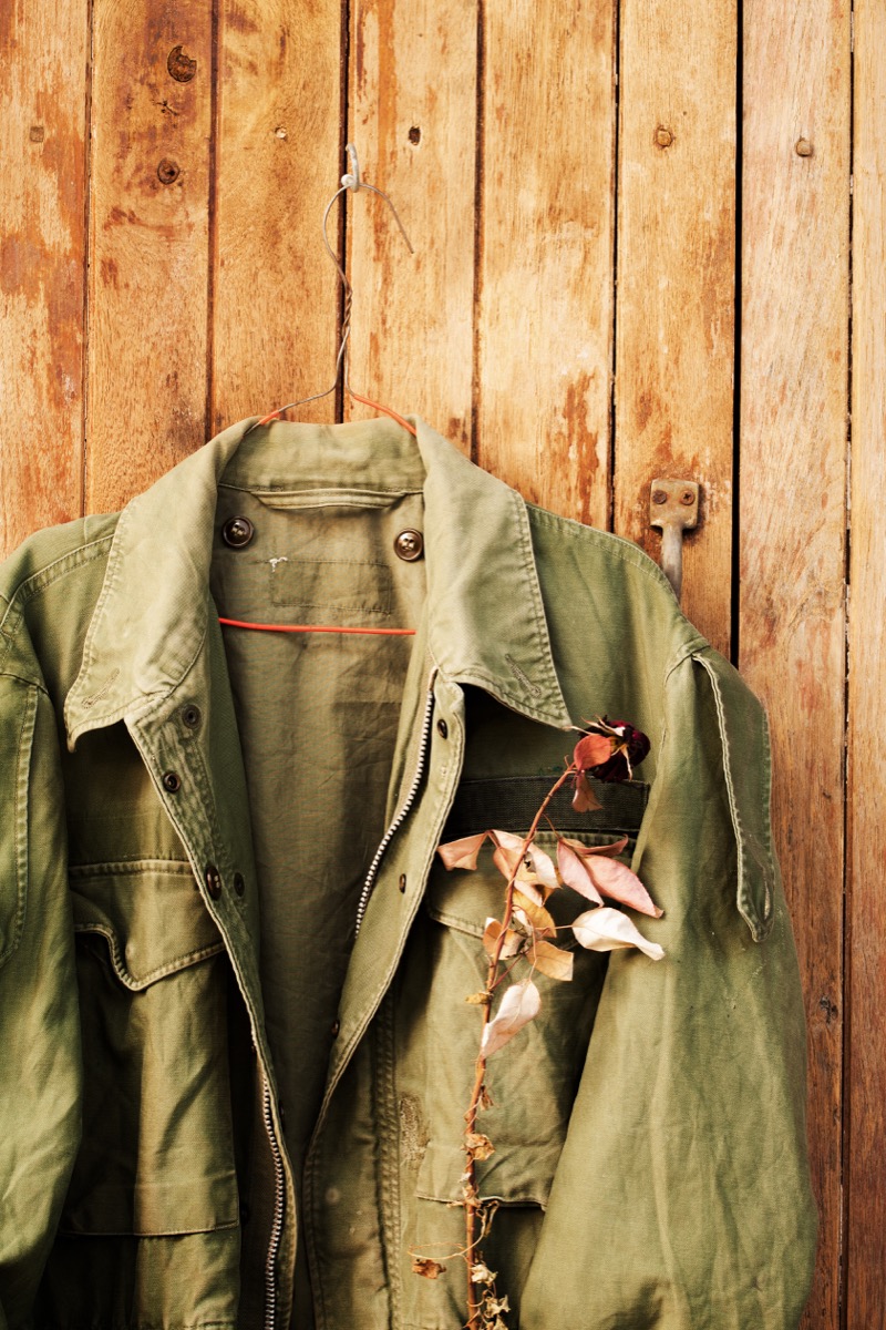 Green army field jacket with dry rose in pocket hang on wood panel - Image