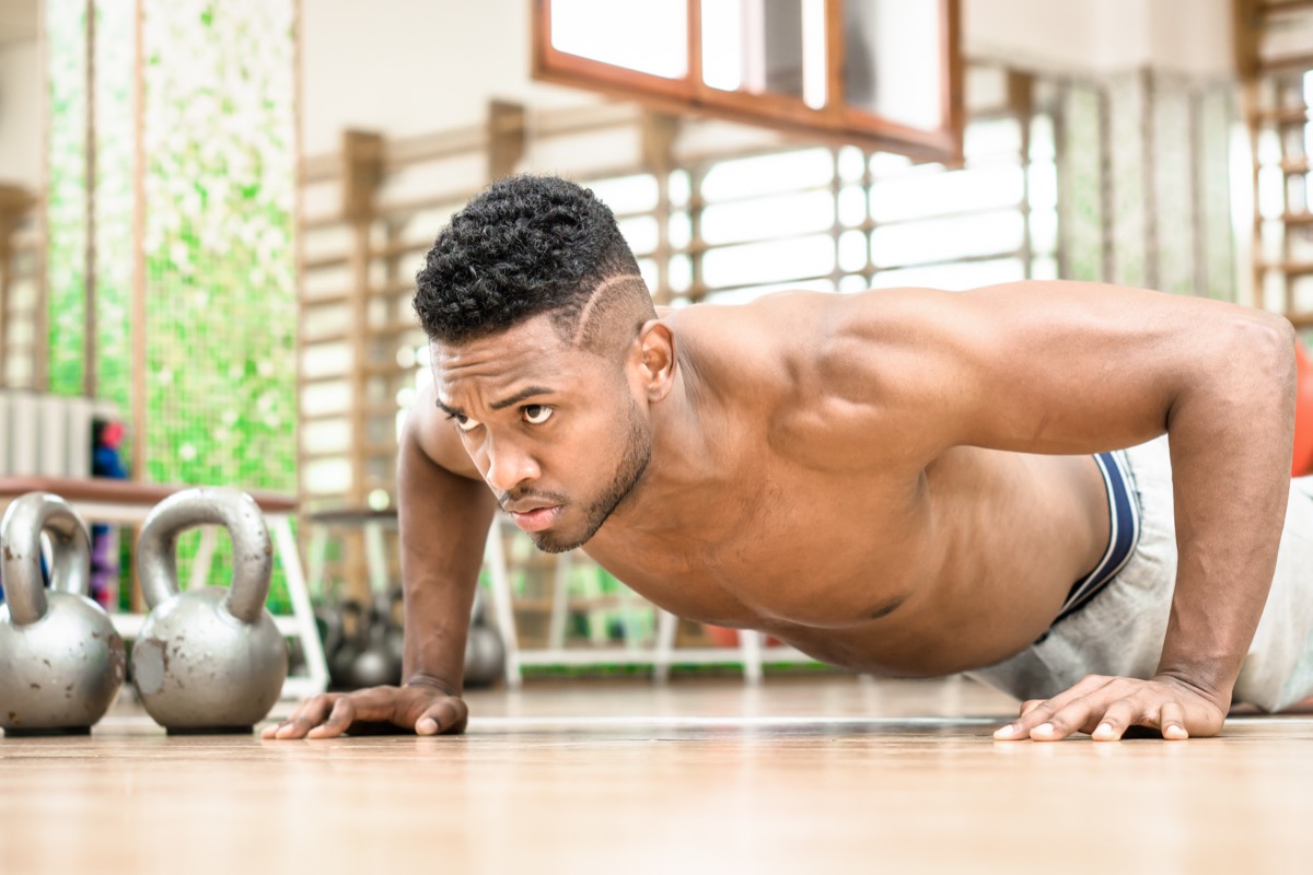 African american man push up chest exercise and gritty serious facial expression inside gym - Attractive black guy shirtless body training muscles on the floor - Concept of sports and fitness indoor - Image