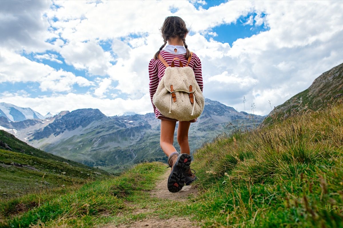 Little girl walks on mountain trail during an excursion. with the backpack. - Image