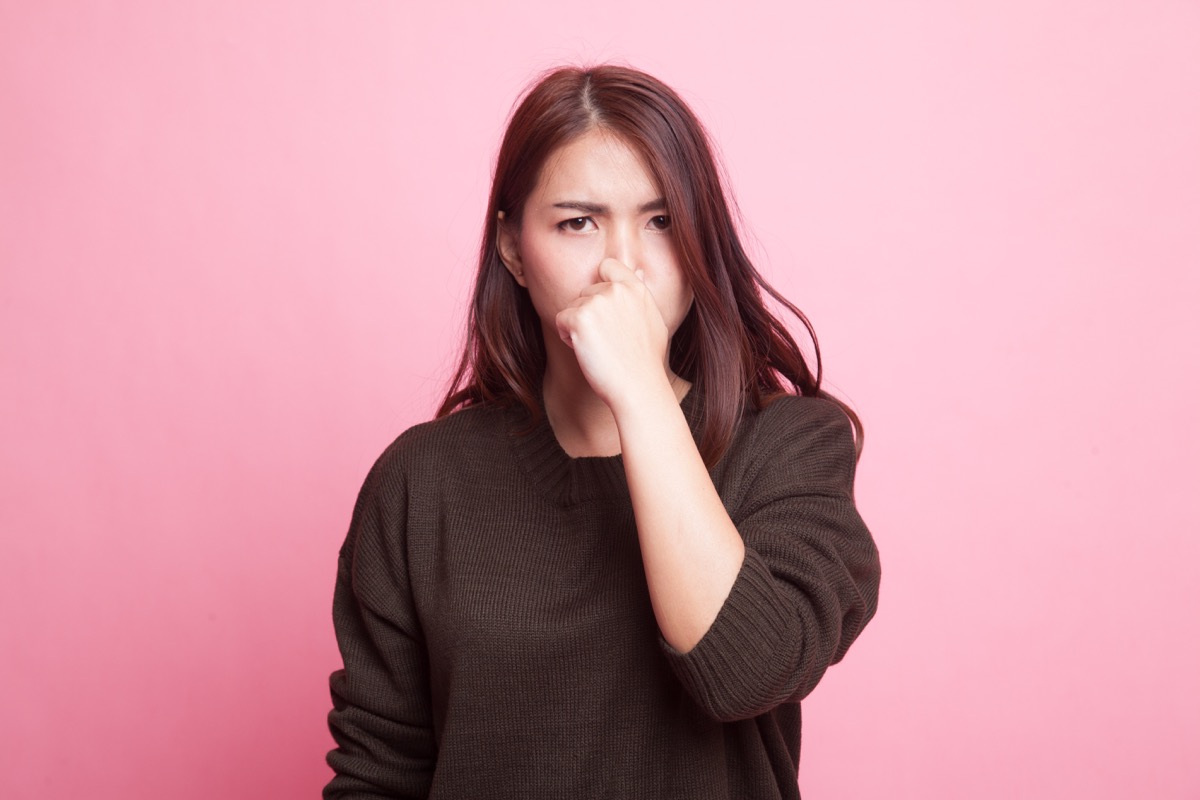Young Asian woman holding her nose because of a bad smell on pink background - Image