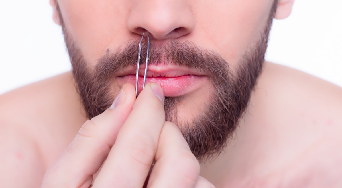 Young handsome bearded man in front of a mirror with tweezers in his hands. - Image
