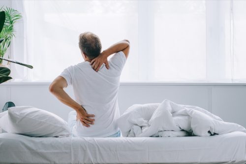 man with back pain sitting on a bed