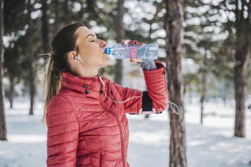 Woman drinking water outside in the winter after going for a jog