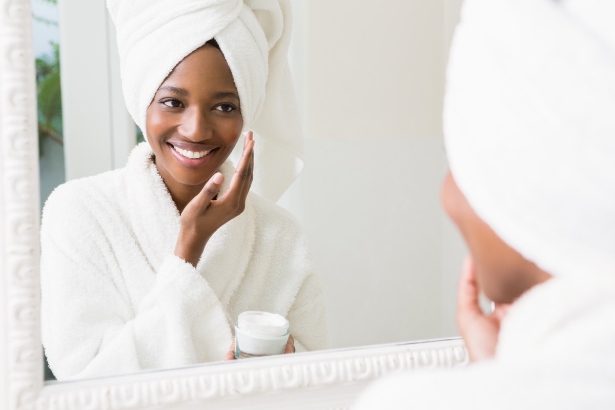 Νεαρή γυναίκα που εφαρμόζει ενυδατική κρέμα στο δέρμα της στο μπάνιο - Εικόνα