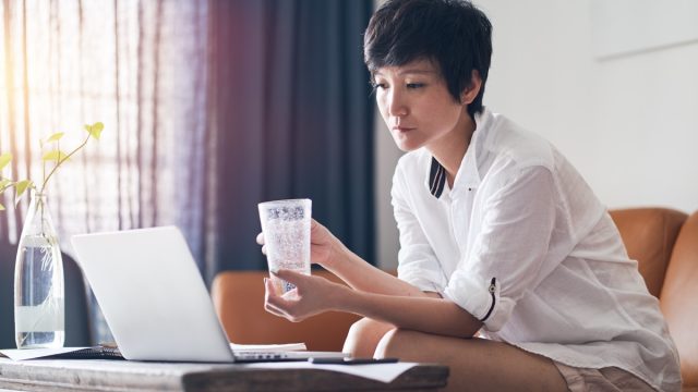 Asian woman drinking a glass of water on the couch, signs your cold is serious