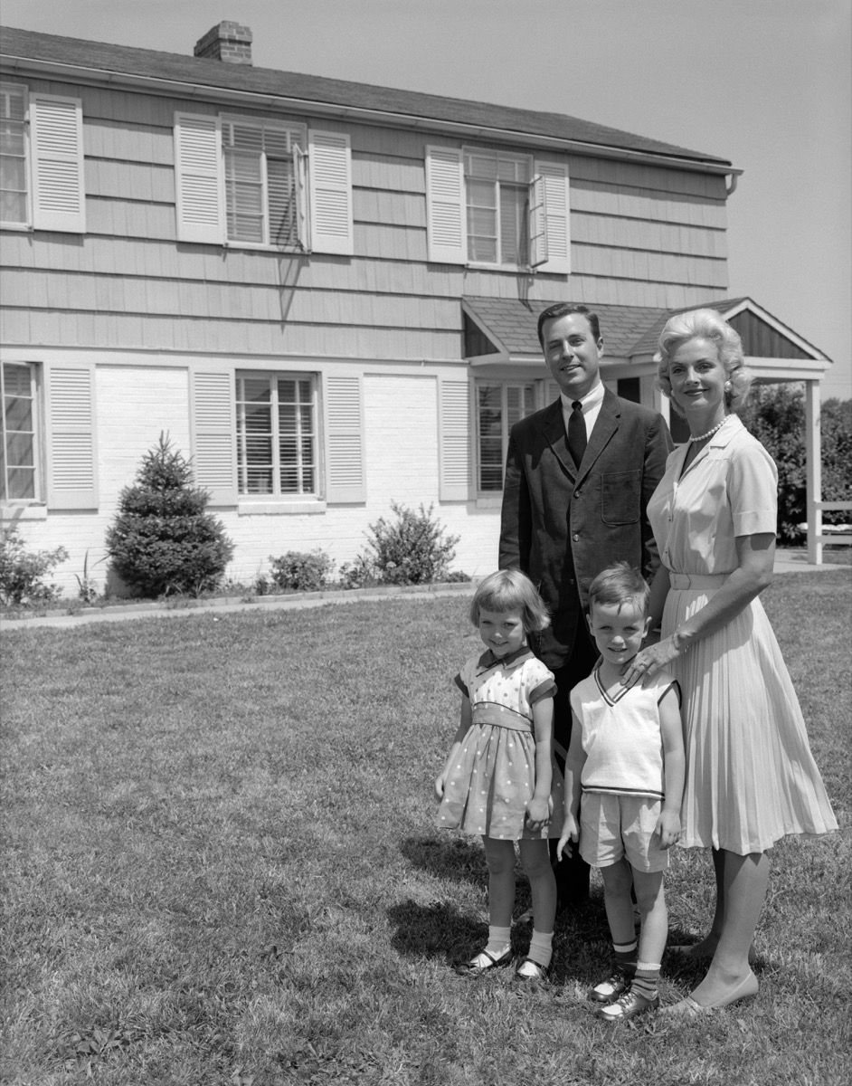 1960s suburban family in black and white photo standing in front of huge suburban home
