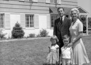 1960s suburban family in black and white photo standing in front of huge suburban home