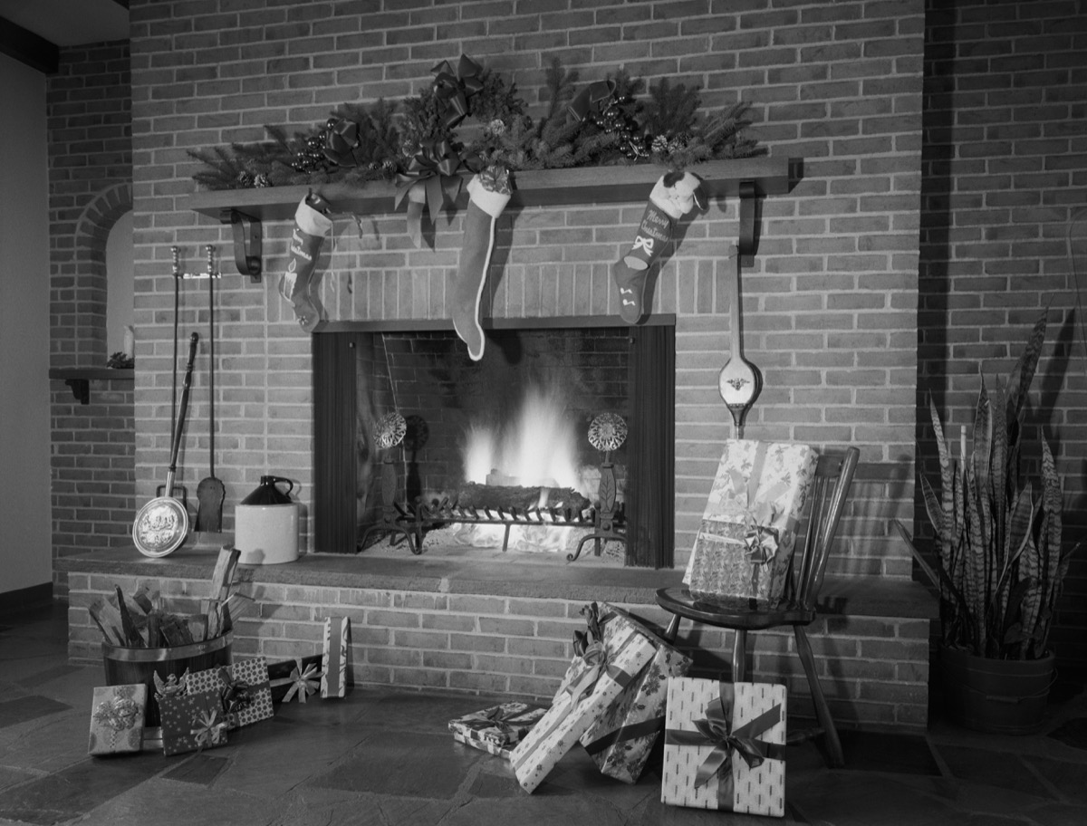 Brick fireplace in black and white photo adorned with stockings and gifts for Christmas in huge house