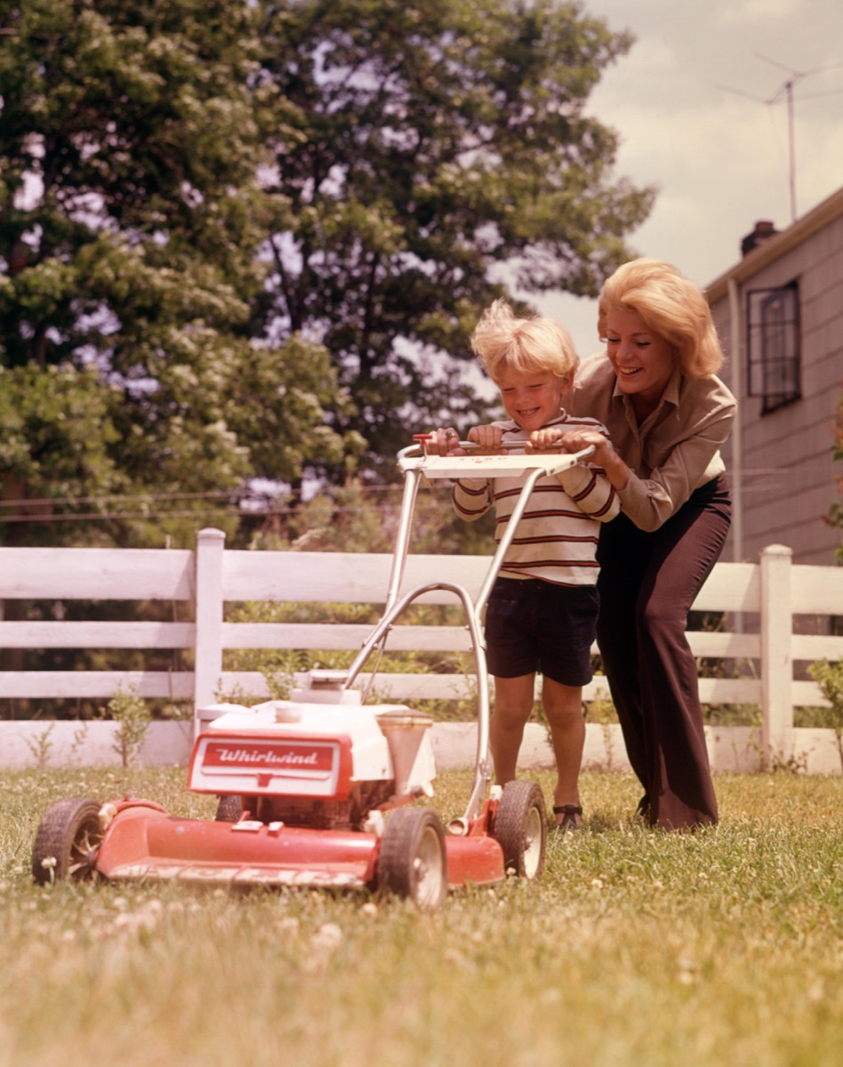 1960s mother and son mow grass at huge house