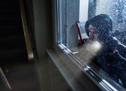 white male burglar holding crowbar and wearing hoodie peering through window of house