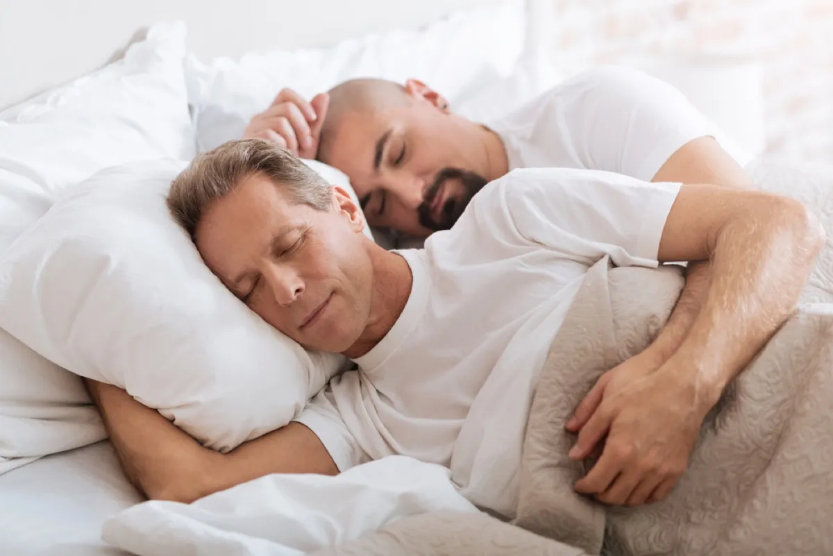 middle age gay couple spoons in bed