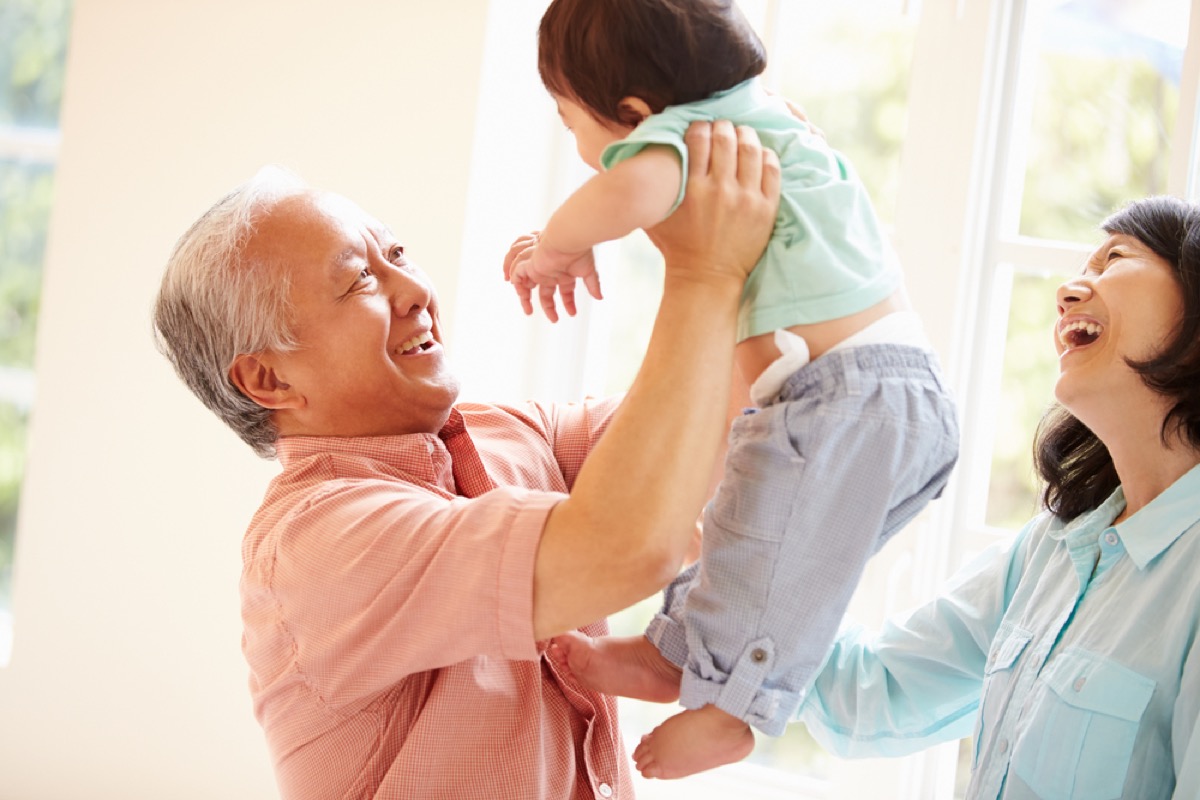 asian grandfather holding grandchild while grandmother looks on