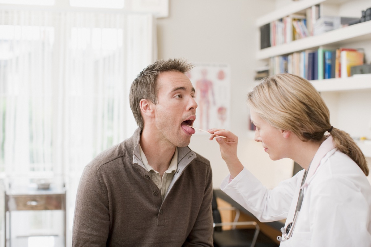 white female doctor using tongue depressor on white man