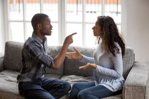 young black man pointing his finger at black woman putting her hands out while they argue on the couch