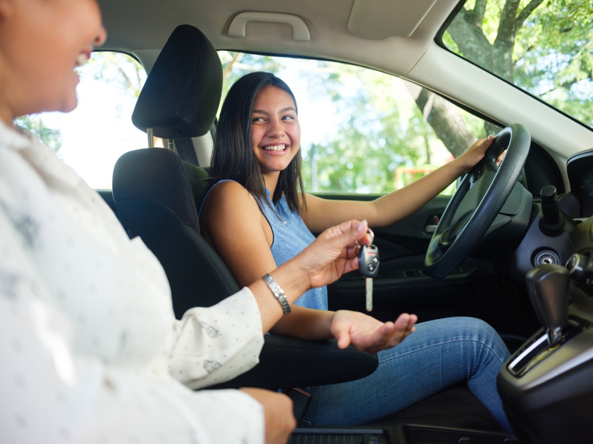 teenage girl driver smiling and getting handed the car keys from her mom